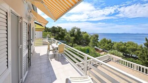 Ein Balkon mit Meerblick, Gartenmöbel und ein gestreifter Sonnenschirm.
