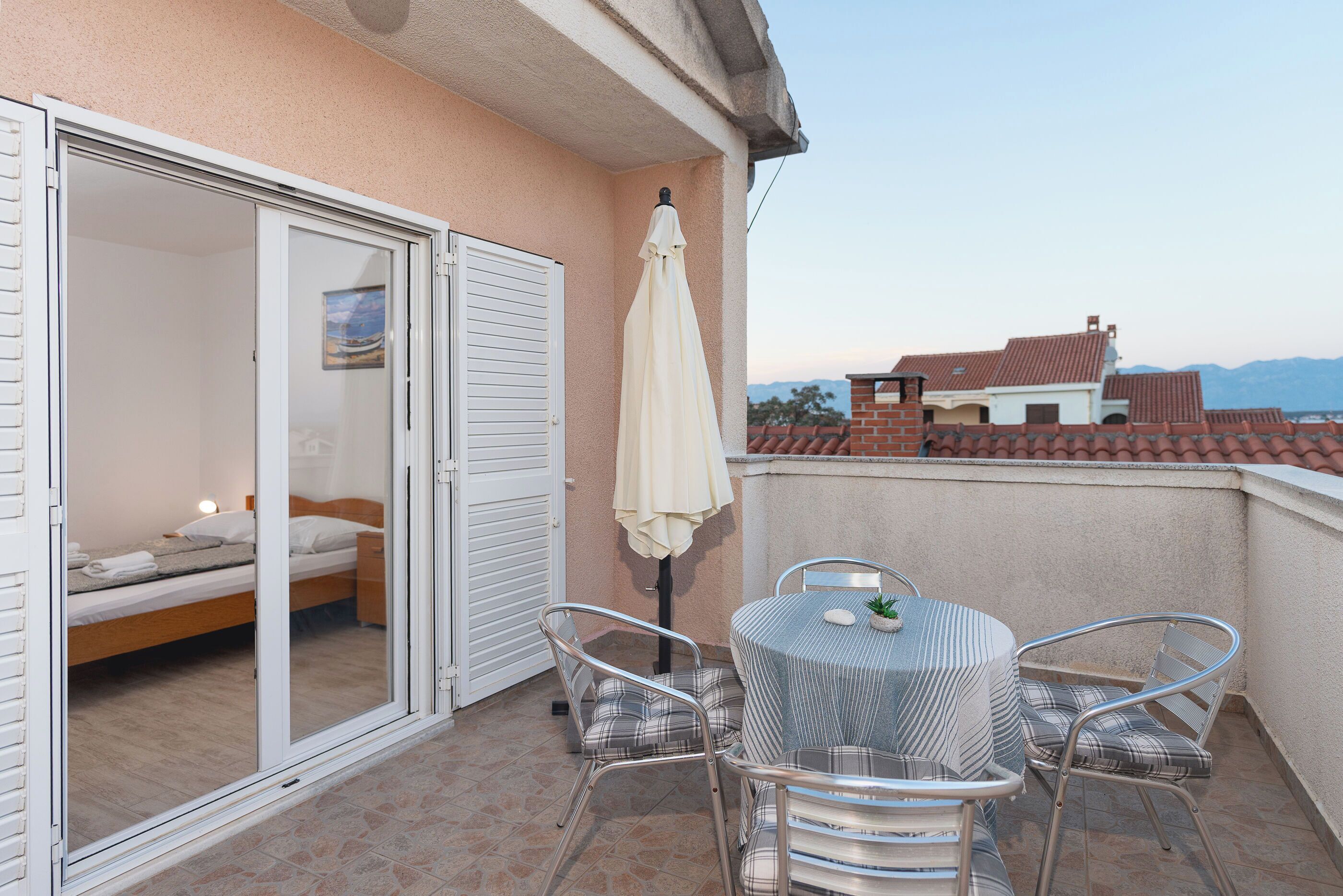 A balcony with a bed, a table with chairs, and a white umbrella.