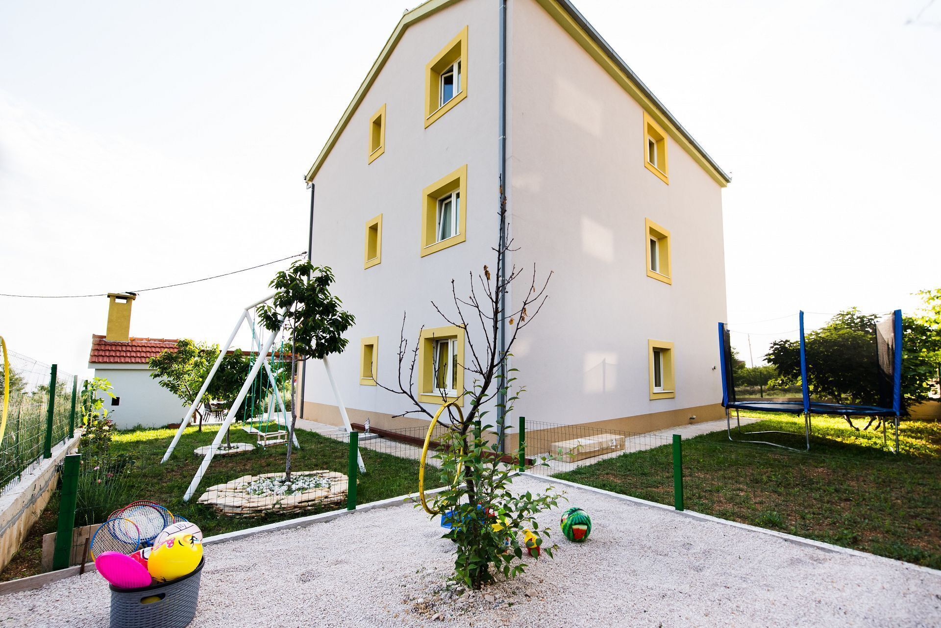 A white building with yellow window frames and a small tree in front.