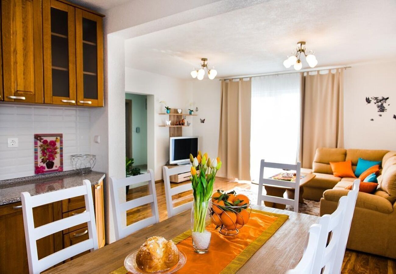 Een moderne keuken met witte kastjes, een eettafel met oranje placemats en een vaas tulpen.