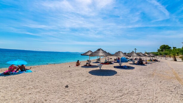 A beach with thatched umbrellas, sun loungers, and a clear blue sky. - Apartment Mariska (Podstrana)