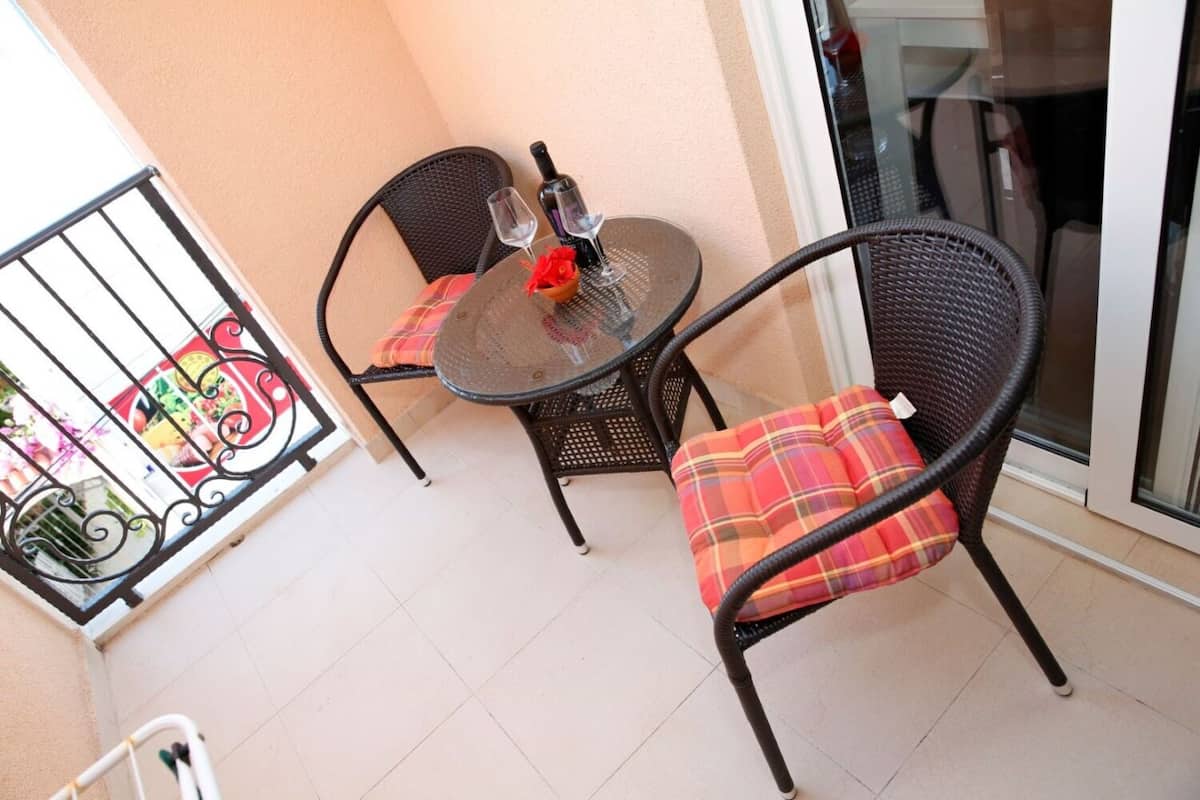 A balcony with two wicker chairs and a glass table, each with a plaid cushion.