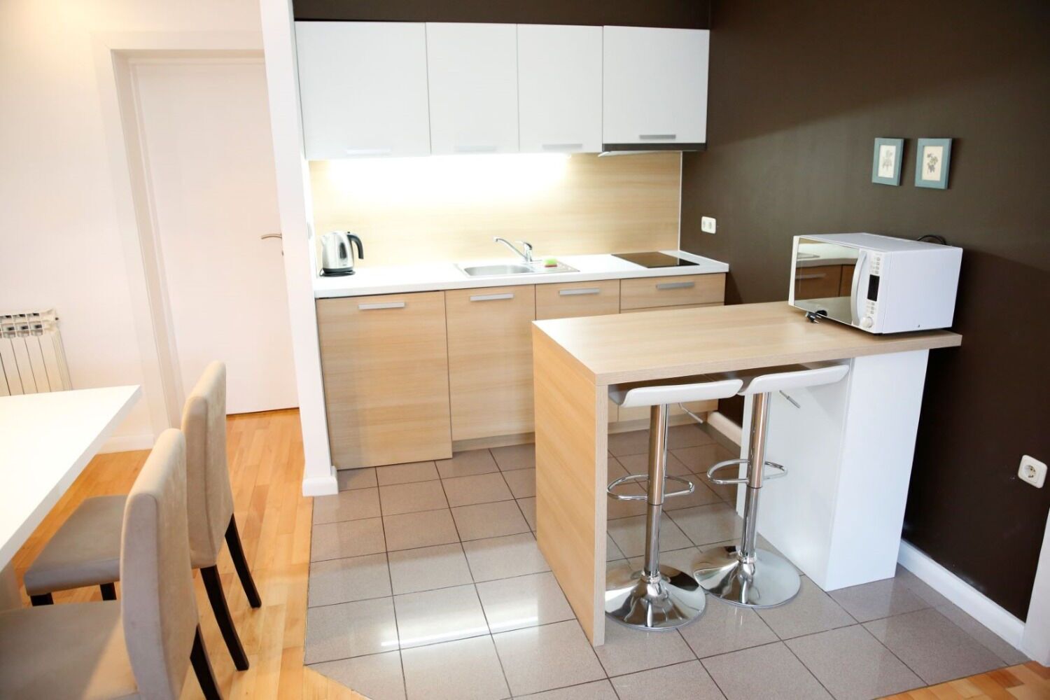 A compact kitchen with a white countertop, a sink, and a microwave. There is a dining area with a white table and chairs.