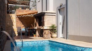 A swimming pool with a stone edge, a wooden deck, and a stone wall. - Apartment Slavena (Okrug)