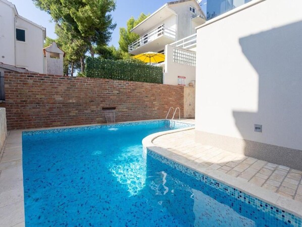 A swimming pool with a tiled edge and a brick wall behind it. - Apartment Slavena (Okrug)