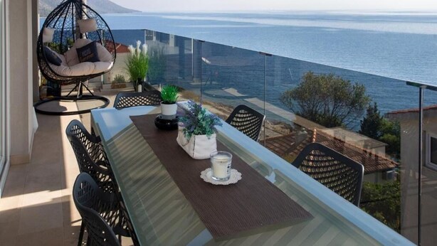 A balcony with a glass table, chairs, and a hanging chair overlooking the sea. - Apartment Slavena (Okrug)