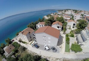 An aerial view of a coastal residential area with buildings, a clear blue sea, and parked cars. - Apartment Slavena (Okrug)
