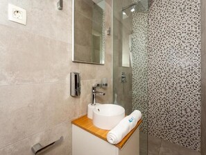 A modern bathroom with a round sink, a mirror, and a shower with a mosaic tile wall. - Apartment Slavena (Okrug)