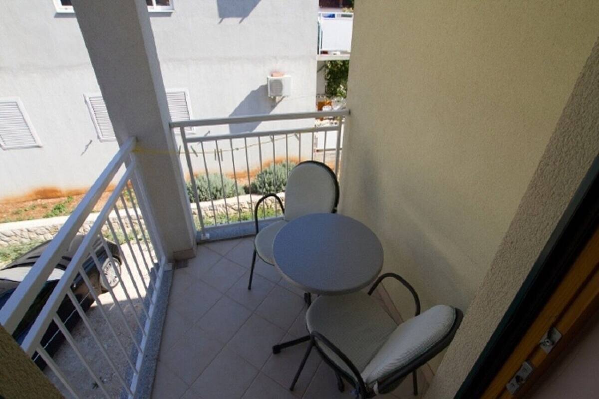 A balcony with a small round table and two chairs, a white railing, and a view of the street below.