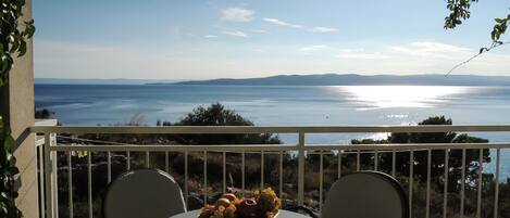 En balkon med et bord og stole, der udover et vandareal og fjerne bakker.