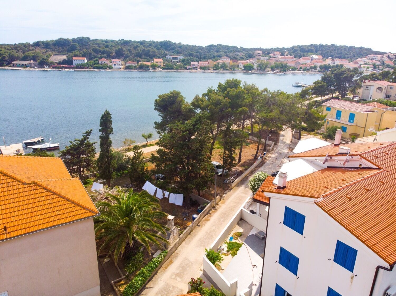 A coastal town with buildings along the waterfront, a clear view of the sea, and a street lined with trees and parked cars.