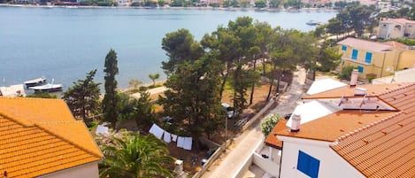 A coastal town with buildings along the waterfront, a clear view of the sea, and a street lined with trees and parked cars.