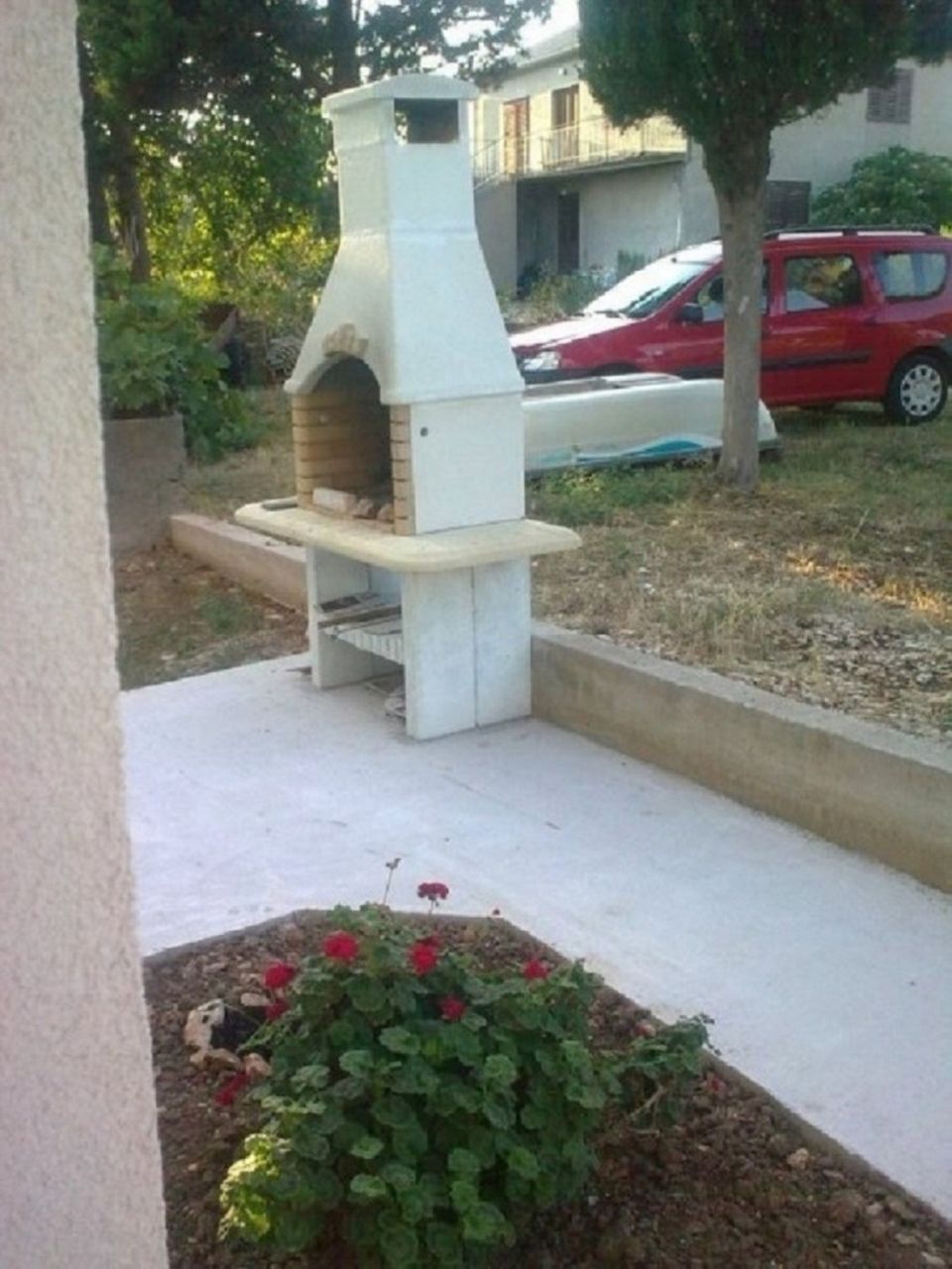 Un horno de ladrillo al aire libre con una chimenea, un banco de hormigón y un jardín de flores rojas.