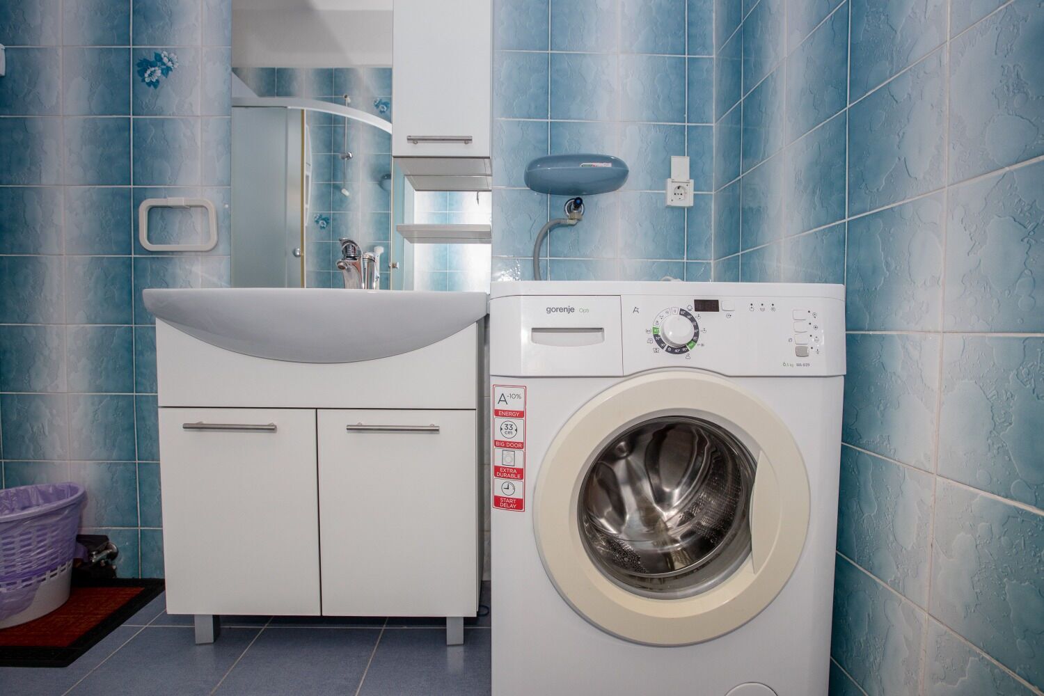 A compact bathroom with a white sink, a washing machine, and a mirror above the sink.