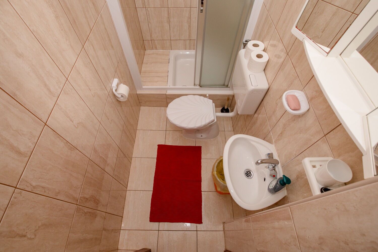 Et badeværelse med toilet, bidet, vask og en rød måtte.