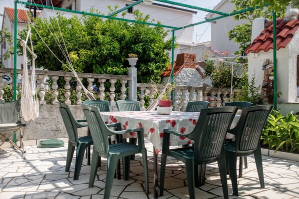 A patio with a table and chairs, surrounded by a white fence and greenery. - Apartments Mili (Rab)