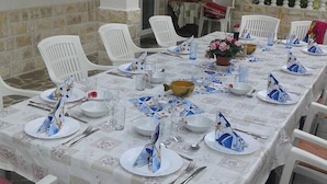 Une table à manger dressée avec des assiettes, des couverts et des verres, entourée de chaises en plastique blanches.