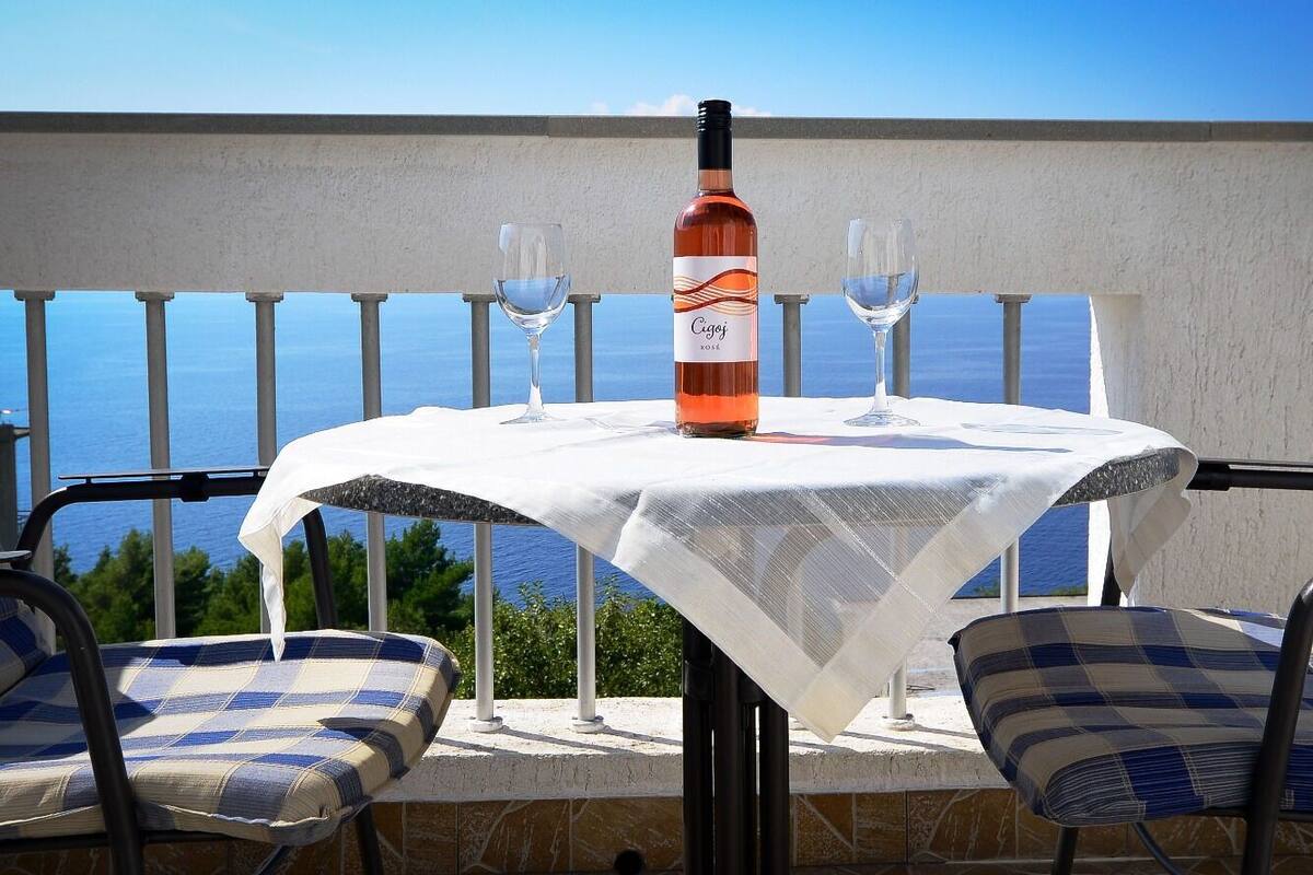 A table with a bottle and glasses on a balcony overlooking the sea.