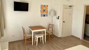 Ein kleiner, gut beleuchteter Raum mit einem Holztisch und zwei Stühlen, einem an der Wand montierten Fernseher und einer Tür mit einem Schild.