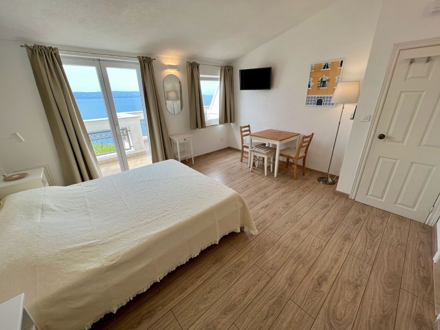 A bedroom with a bed, a small table, two chairs, a TV, and a window with curtains.