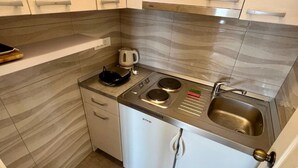 Eine kompakte Küche mit weißen Schränken, einem eingebauten Backofen, einer Spüle und einem kleinen Hocker.