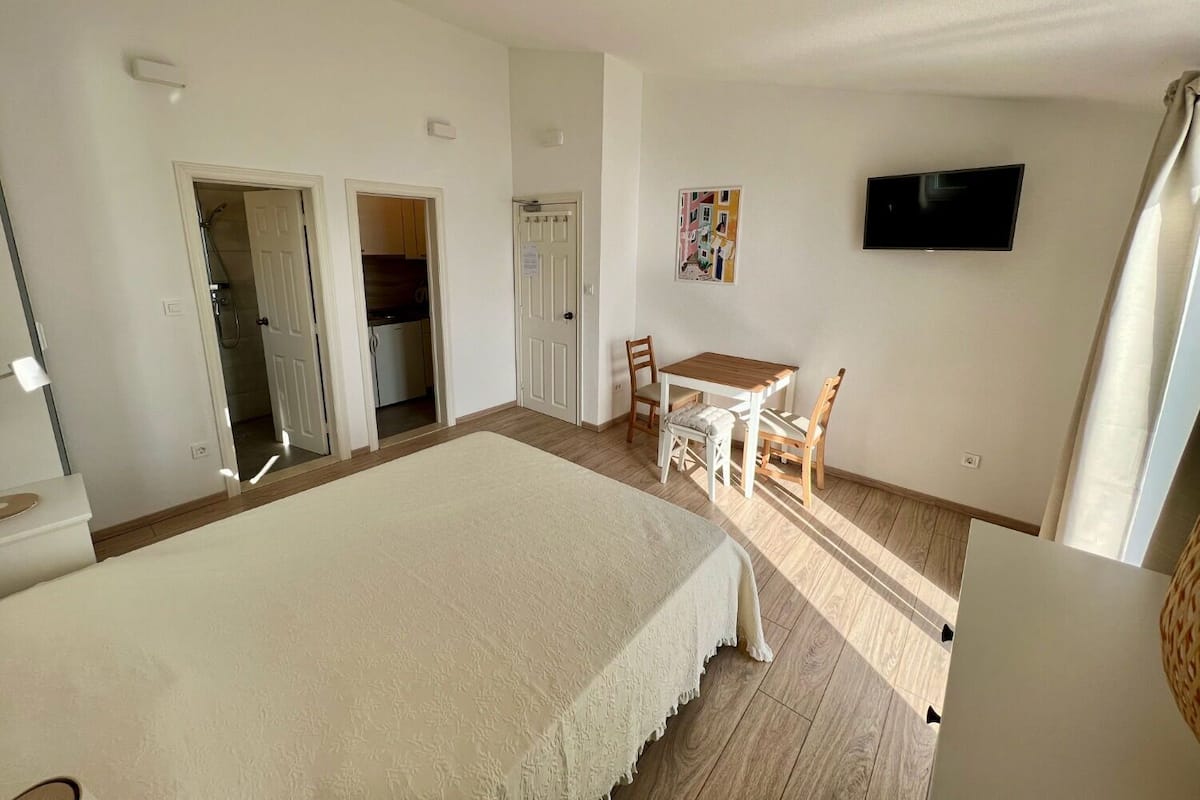 A bedroom with a large bed, a desk with two chairs, a television, and a bathroom visible through an open door.