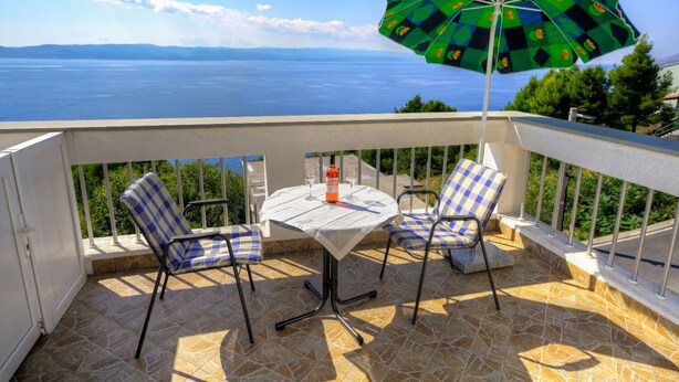 Ein Balkon mit Tisch und zwei Stühlen mit Blick auf ein Gewässer.