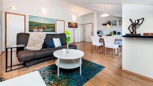 Ein modernes Wohnzimmer mit einer Couch, einem Couchtisch und einem Essbereich mit Stühlen. Im Hintergrund ist eine Küche zu sehen.