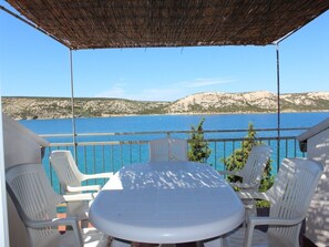 A balcony with a table and chairs overlooking a beach and sea. - Apartments Ljubo (Novalja)