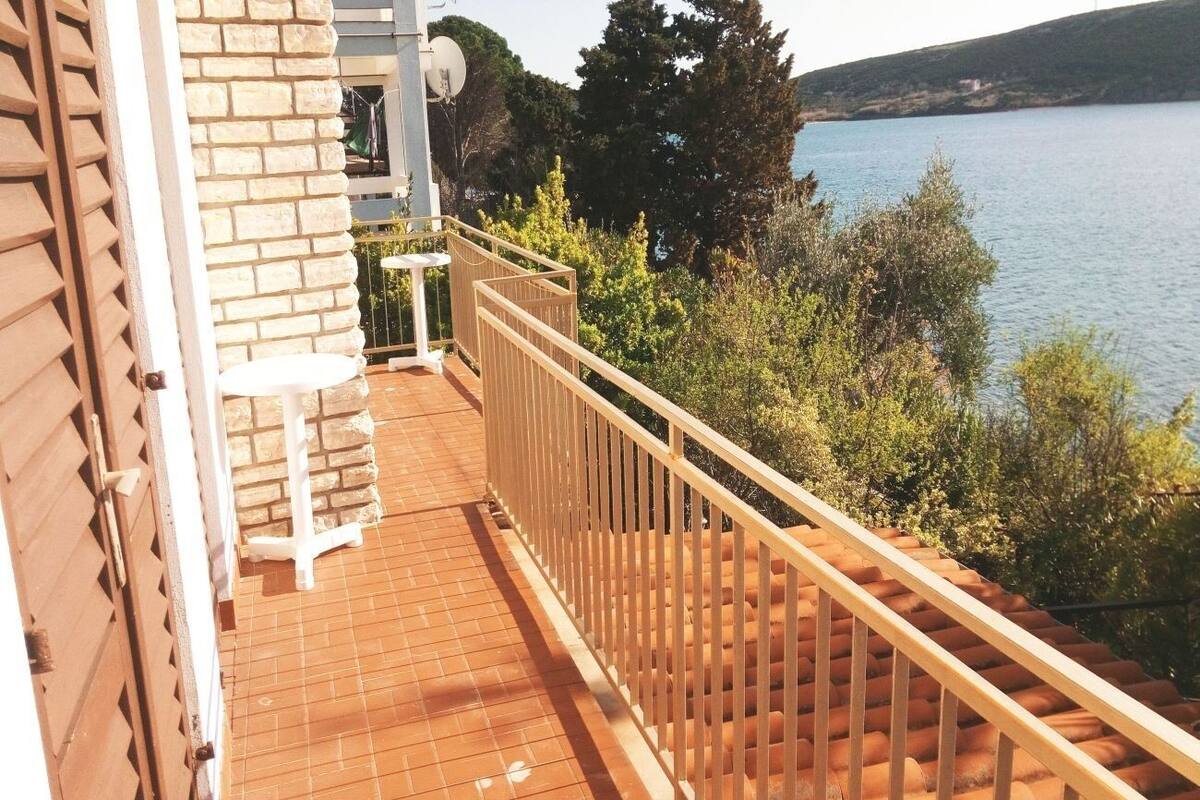 A balcony with a tiled floor, a white chair, and a railing overlooking a body of water and greenery.