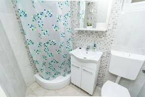 A bathroom with a shower, toilet, sink, and a small shelf with a plant. - House Vers (Vela Luka)