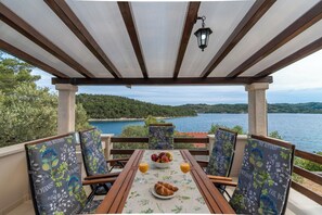 A covered outdoor seating area with a table set for two, featuring a view of a lake and hills. - House Vers (Vela Luka)
