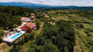 An aerial view of a residential area with houses, a swimming pool, and surrounding greenery. - House Brapa (Hrvace)
