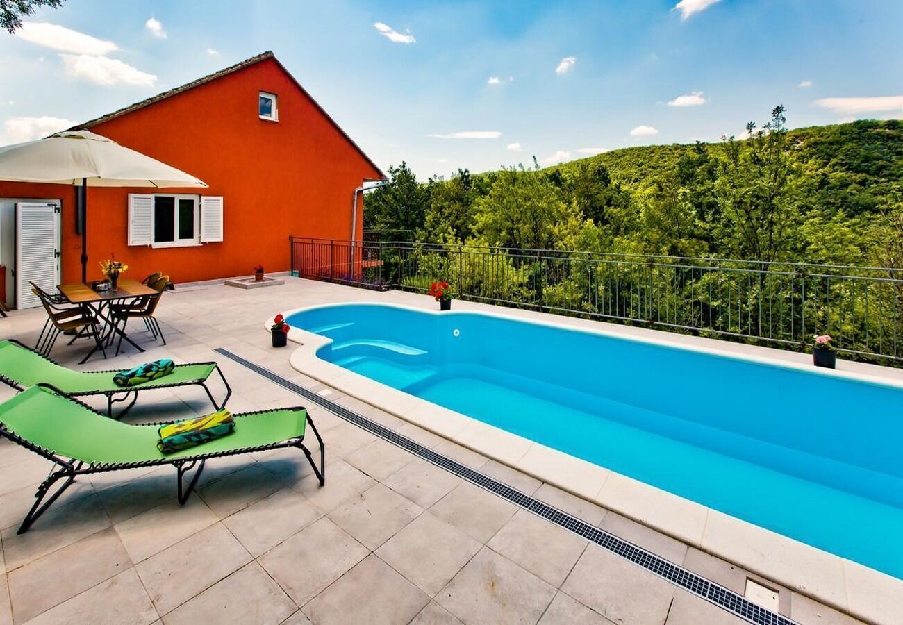 A swimming pool with lounge chairs, a red building, and a green landscape in the background.