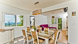 A modern dining area with a glass table, wooden chairs, and a view of the outdoors through large windows. - House Brapa (Hrvace)