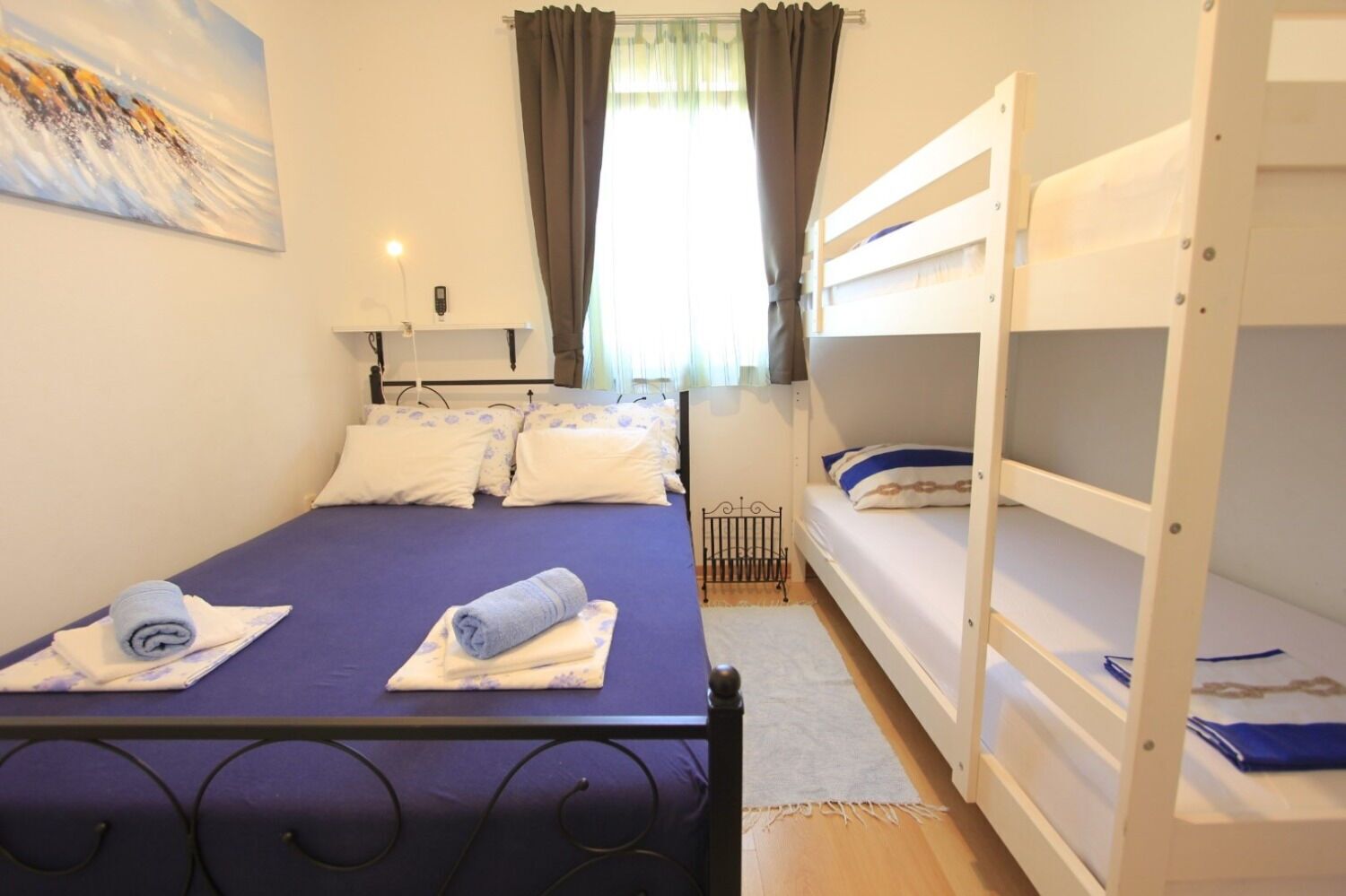 A room with a bed, a bunk bed, a painting on the wall, and a window with curtains.