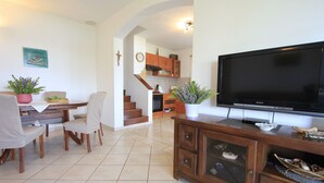 A living room with a TV, wooden furniture, a dining area with chairs and a table, and a kitchen in the background. - House Mirta (Sali)