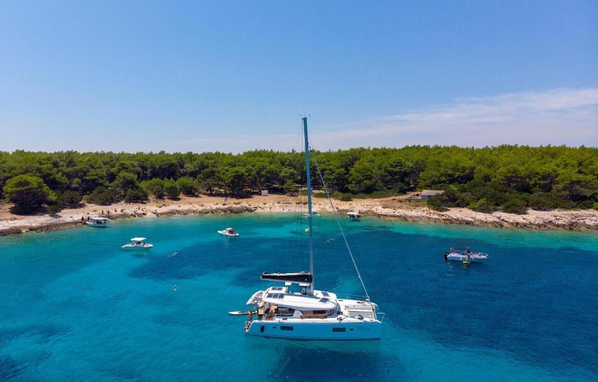 A large yacht anchored in clear turquoise waters with a forested coastline in the background.