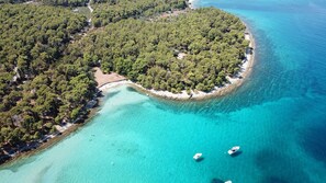 Luchtbeeld van een klein eiland met helder turquoise water, omringd door dichtgroene begroeiing. Enkele boten liggen afgemeerd bij de kust.