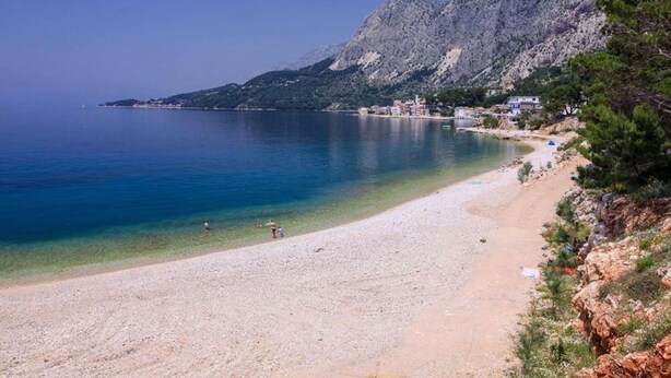 A beach with clear water, a rocky mountain in the background, and buildings along the shore. - Apartments Ivi (Podgora)