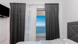 A bedroom with a bed, a TV mounted on the wall, and a view of the sea through the window. - Apartments Ivi (Podgora)