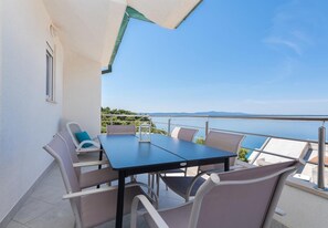 A balcony with a table and chairs, overlooking a body of water and distant land. - Apartments Ivi (Podgora)