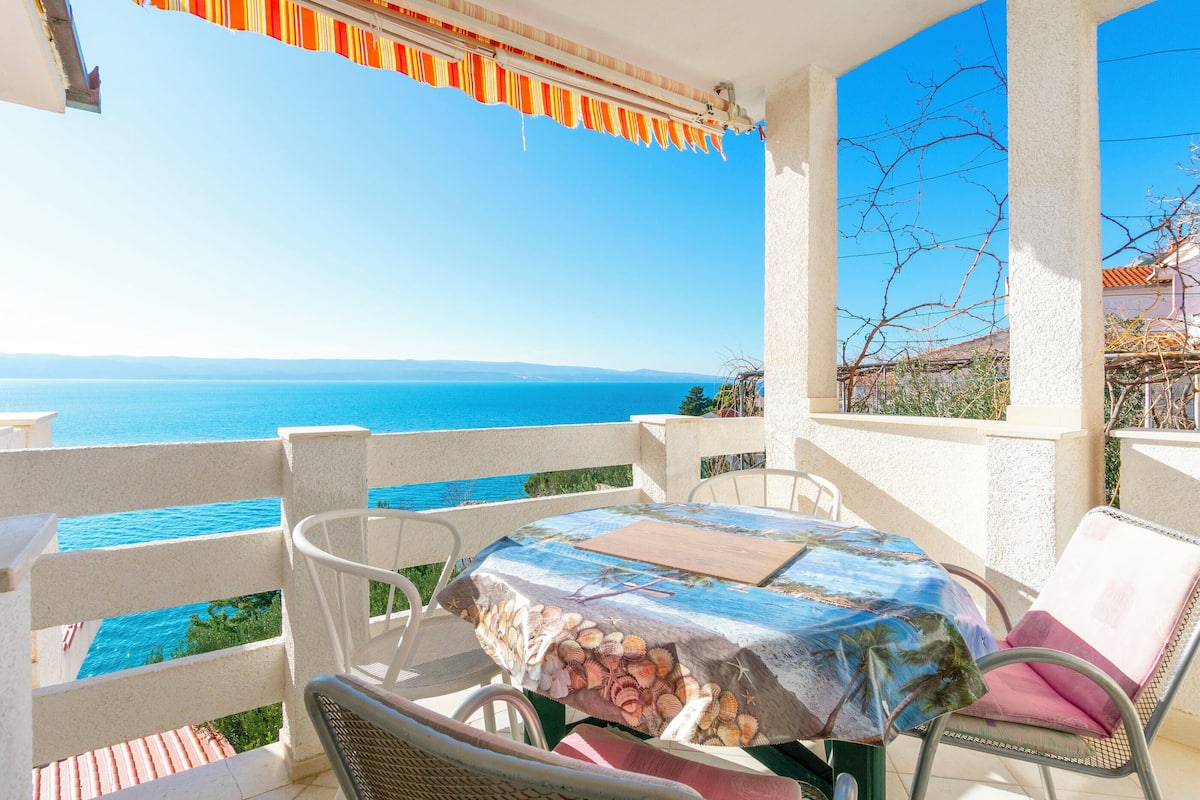 A balcony with a table and chairs overlooking a sea view.