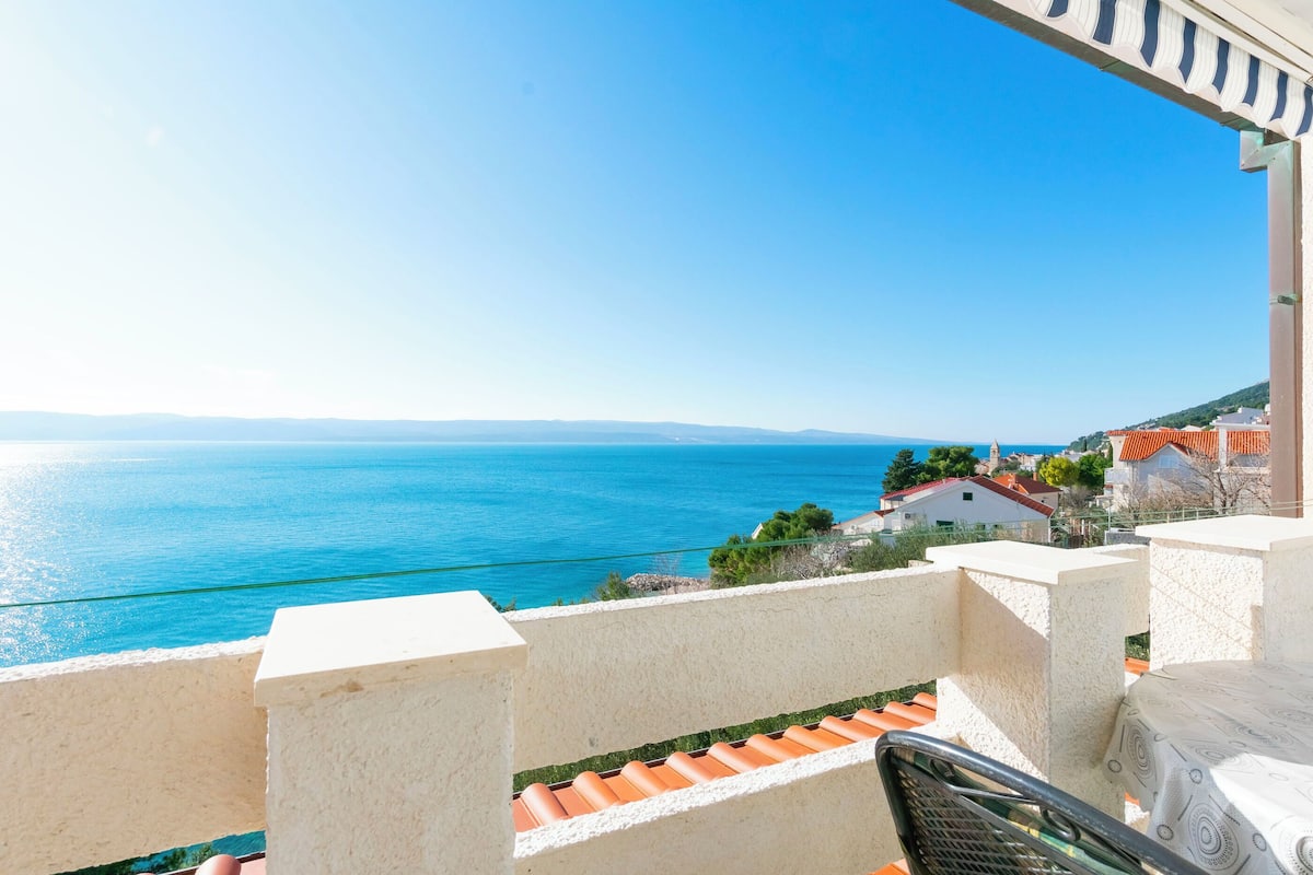 A balcony with a view of the sea and houses in the background.