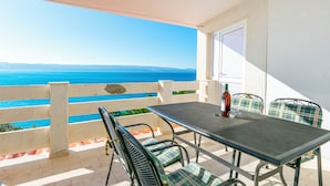 A balcony with a table and chairs, overlooking a coastal view. - Apartments Ivo (Omis)