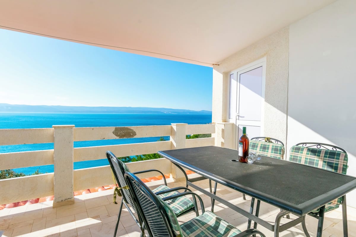 A balcony with a table and chairs, overlooking a coastal view.