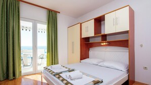 A bedroom with a bed, a wardrobe, and a view of the sea through a sliding door. - Apartments Ivo (Omis)