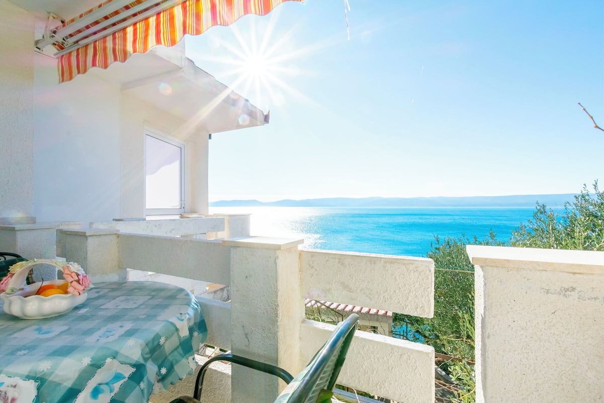 A balcony with a view of the sea, a small table with a basket, and a window.