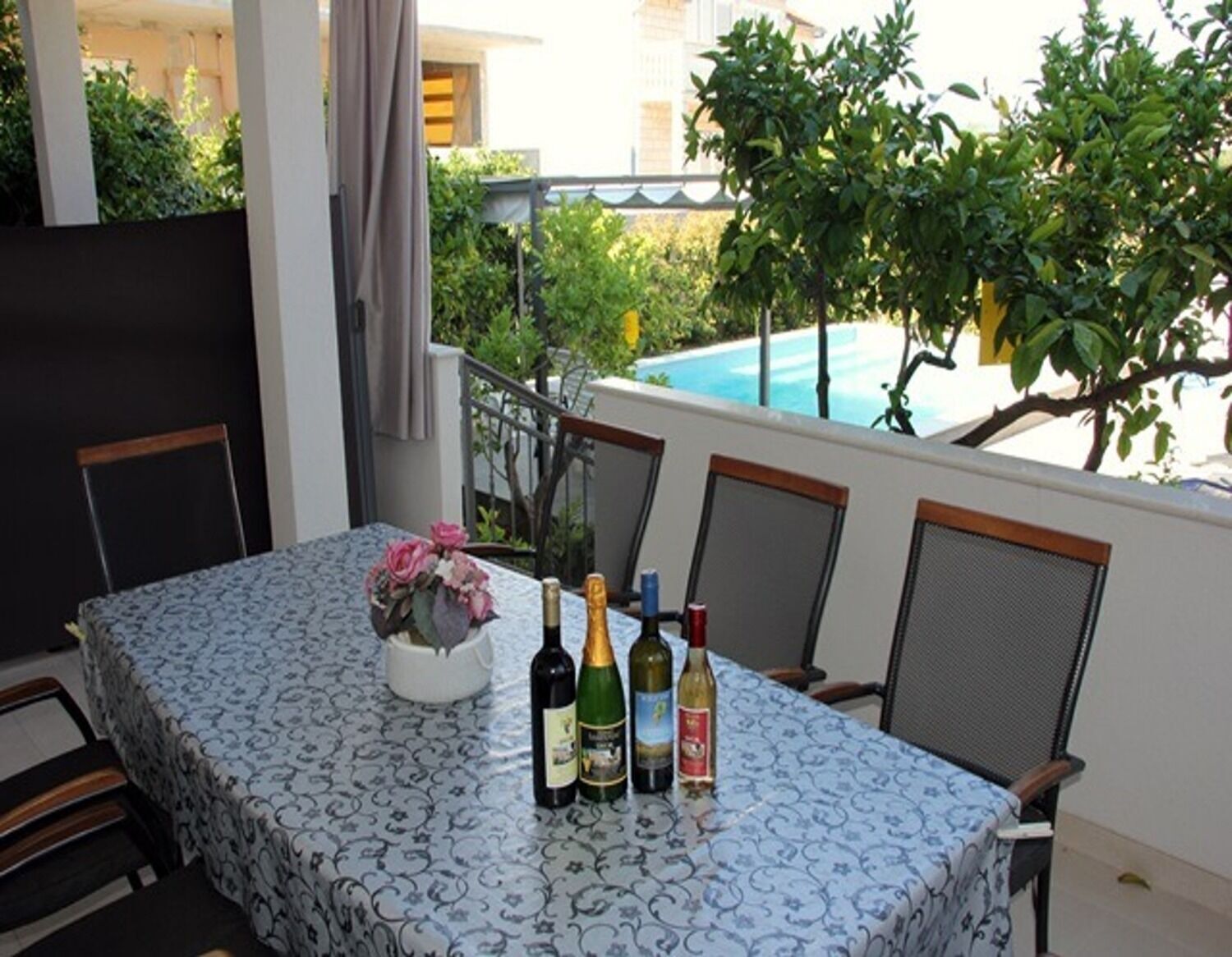 A table set for four with a floral centerpiece, four bottles of wine, and a glass of water on a balcony overlooking a pool.