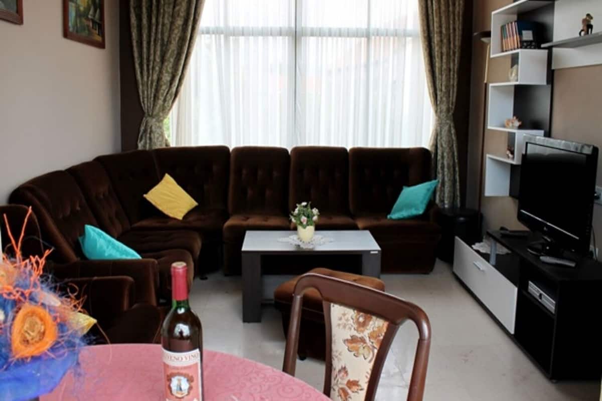 A living room with a brown sofa, a coffee table, a TV, and a bottle of wine.